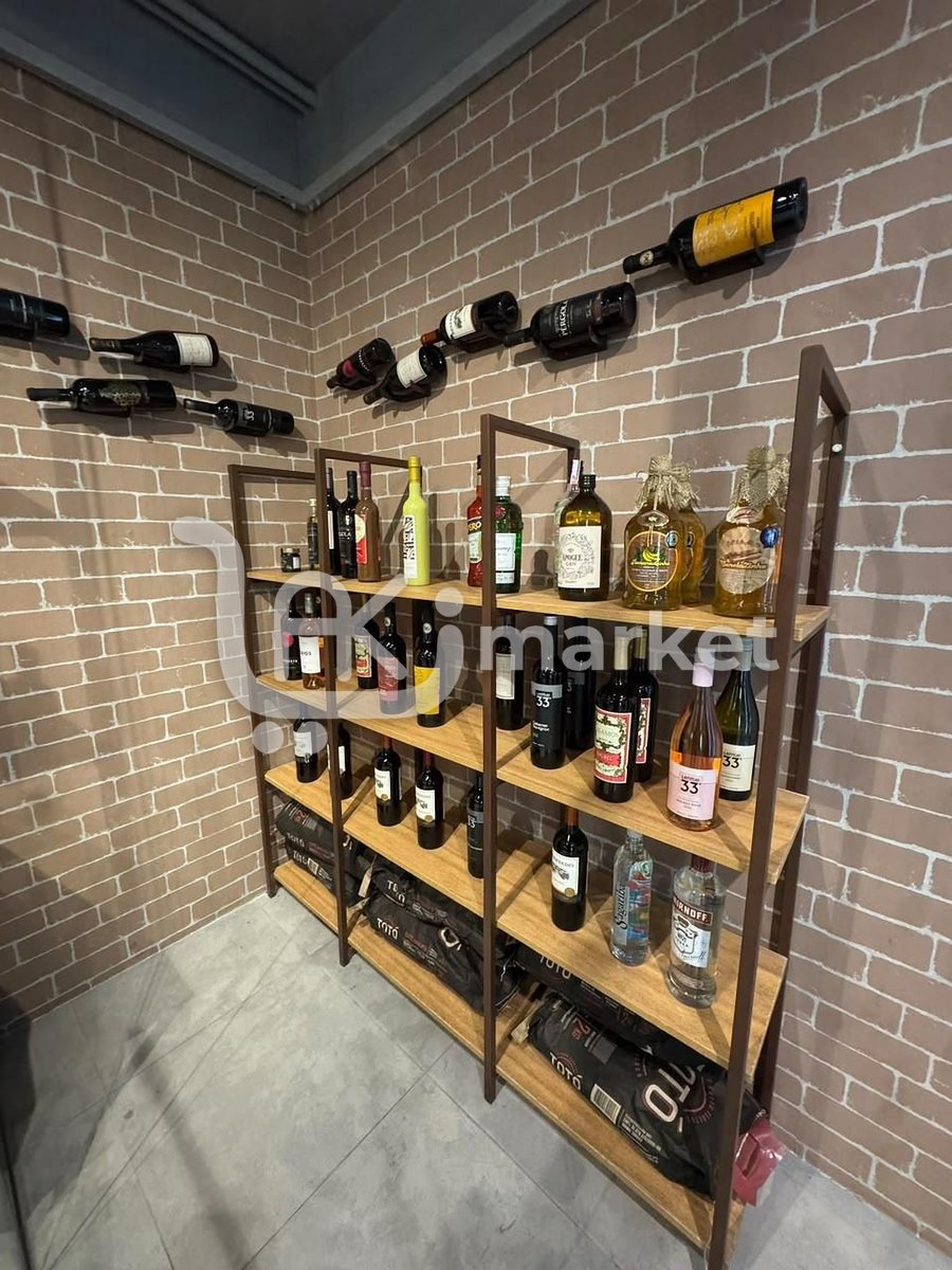 Adega com garrafas de vinho penduradas na parede de tijolinhos e prateleiras de madeira com bebidas.